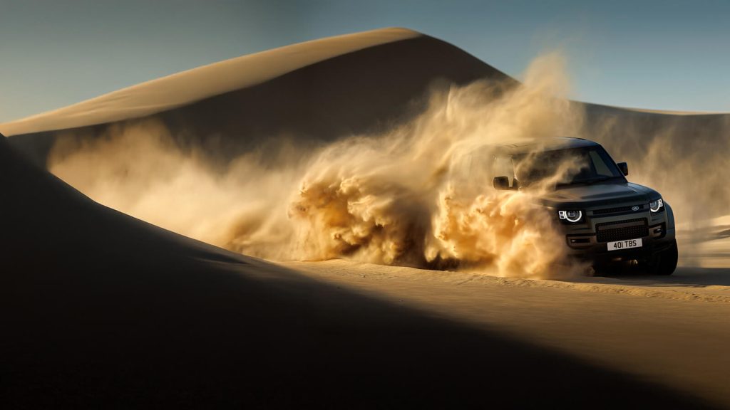 2025 Defender 110 P300 driving through desert sand.